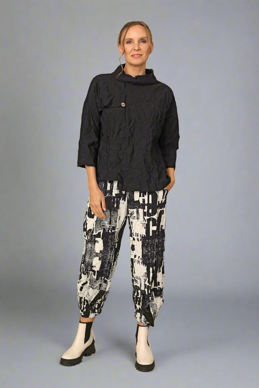 Person wearing a black jacket and patterned pants on a gray background
