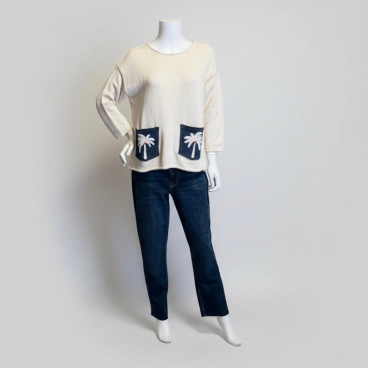 Mannequin wearing a cream sweater with palm tree designs and dark blue jeans on a light gray background