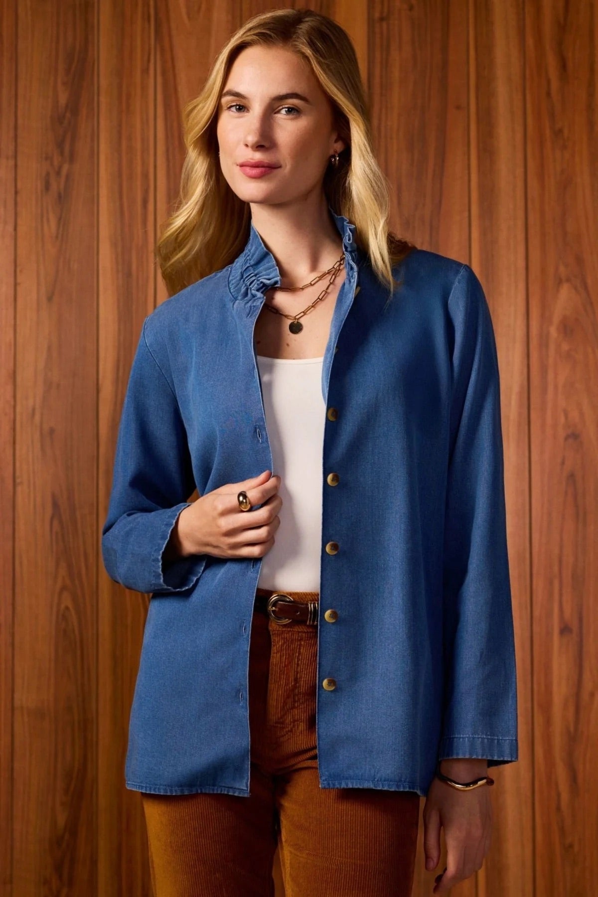 Woman wearing a blue jacket over a white top and brown pants against a wooden background