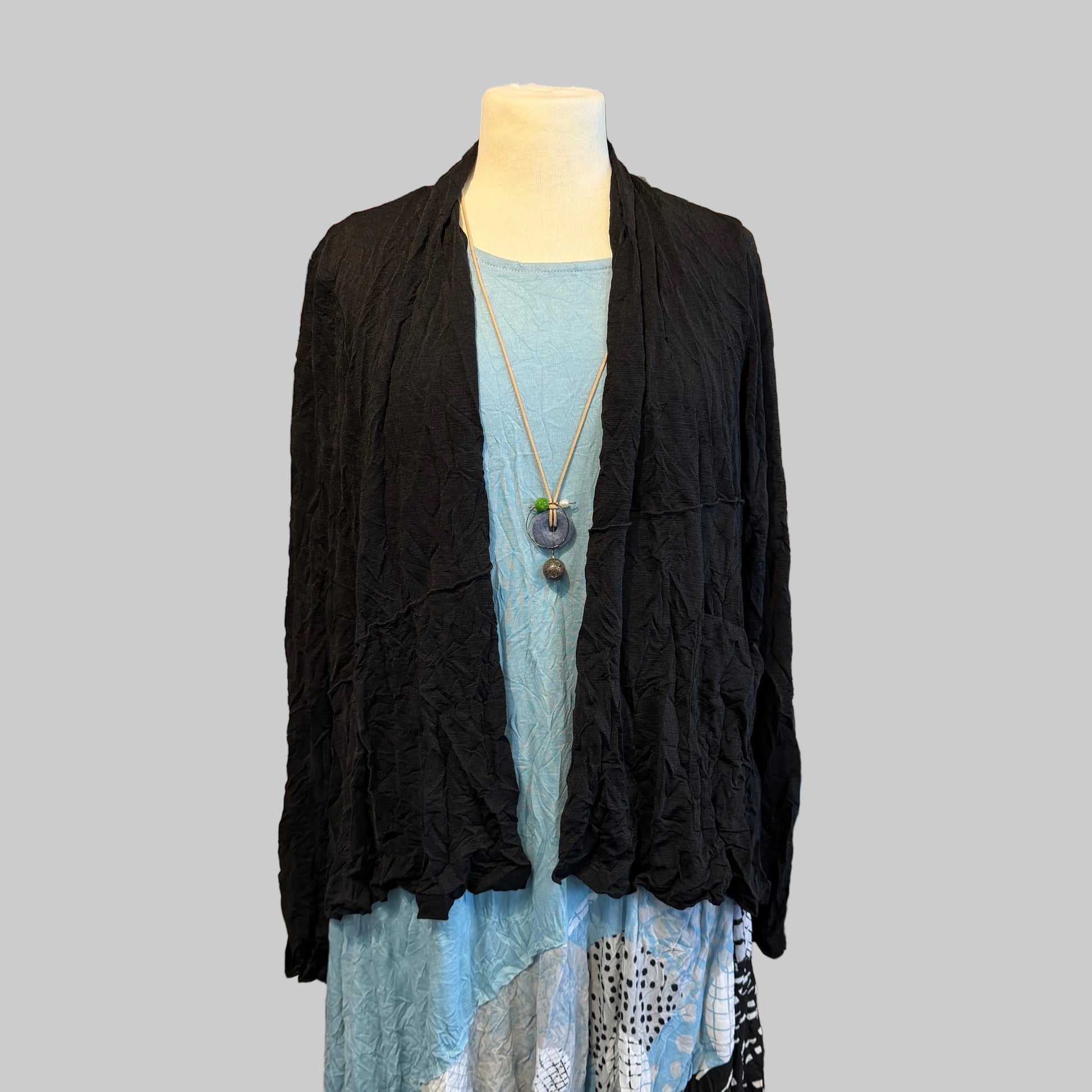 Mannequin wearing a black cardigan and blue dress with a white shelf displaying various items in the background.