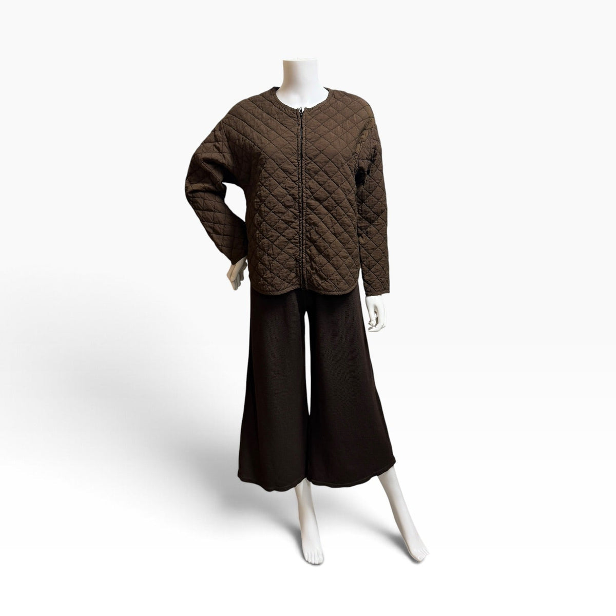A dark brown quilted jacket with a front zipper, displayed on a white mannequin torso alongside dark brown wide-leg cropped pants against a clean white studio background.