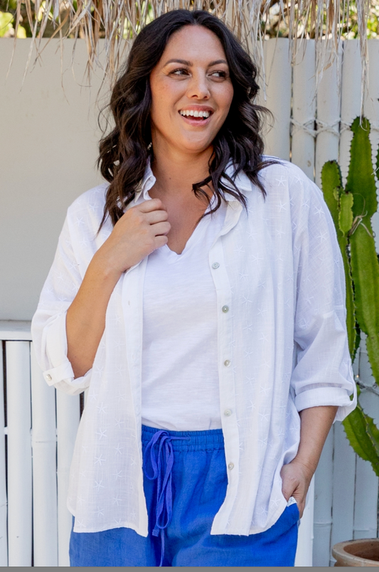 Woman wearing a white shirt and blue pants standing outdoors with a cactus plant in the background.