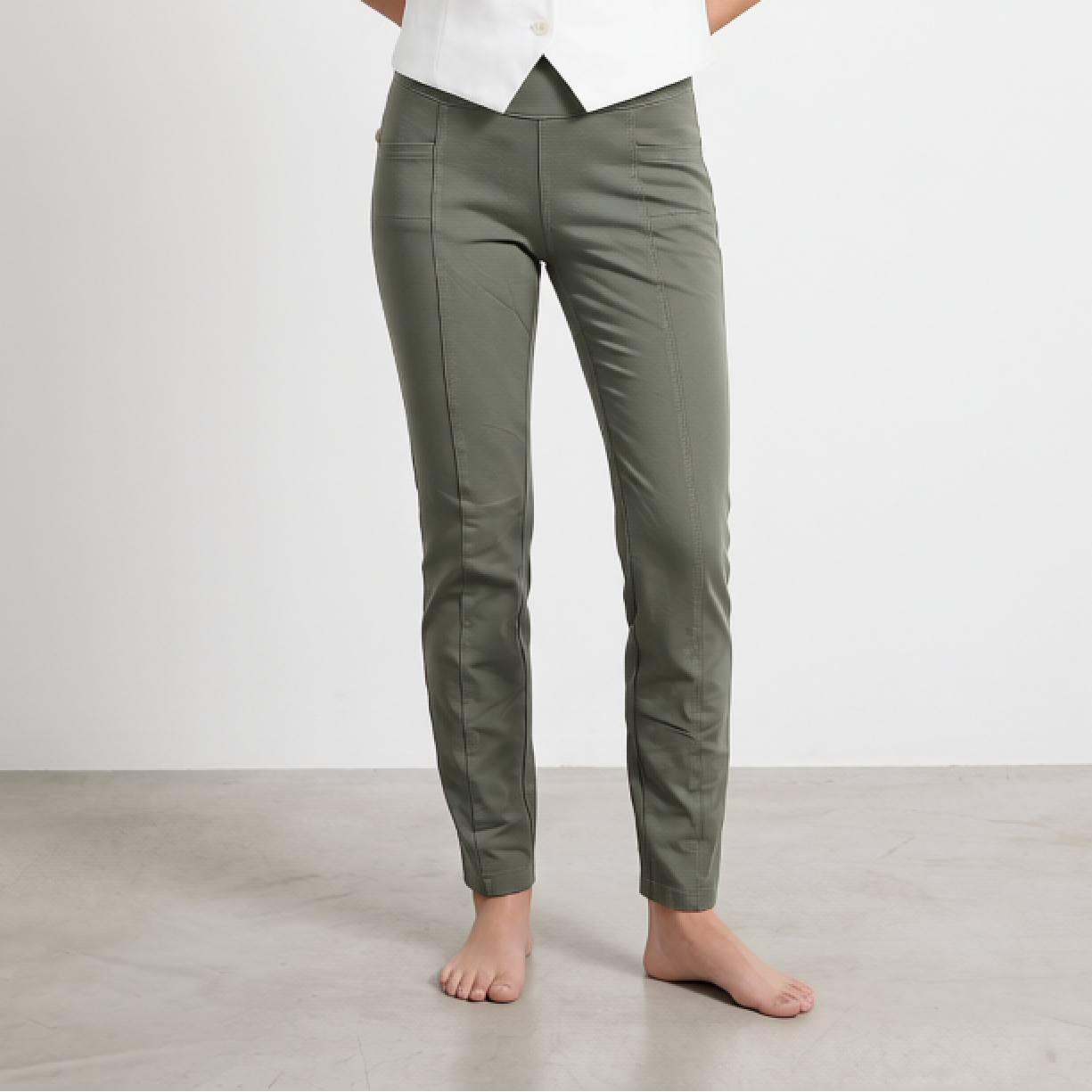 Woman wearing a white sleeveless top and green pants against a plain background