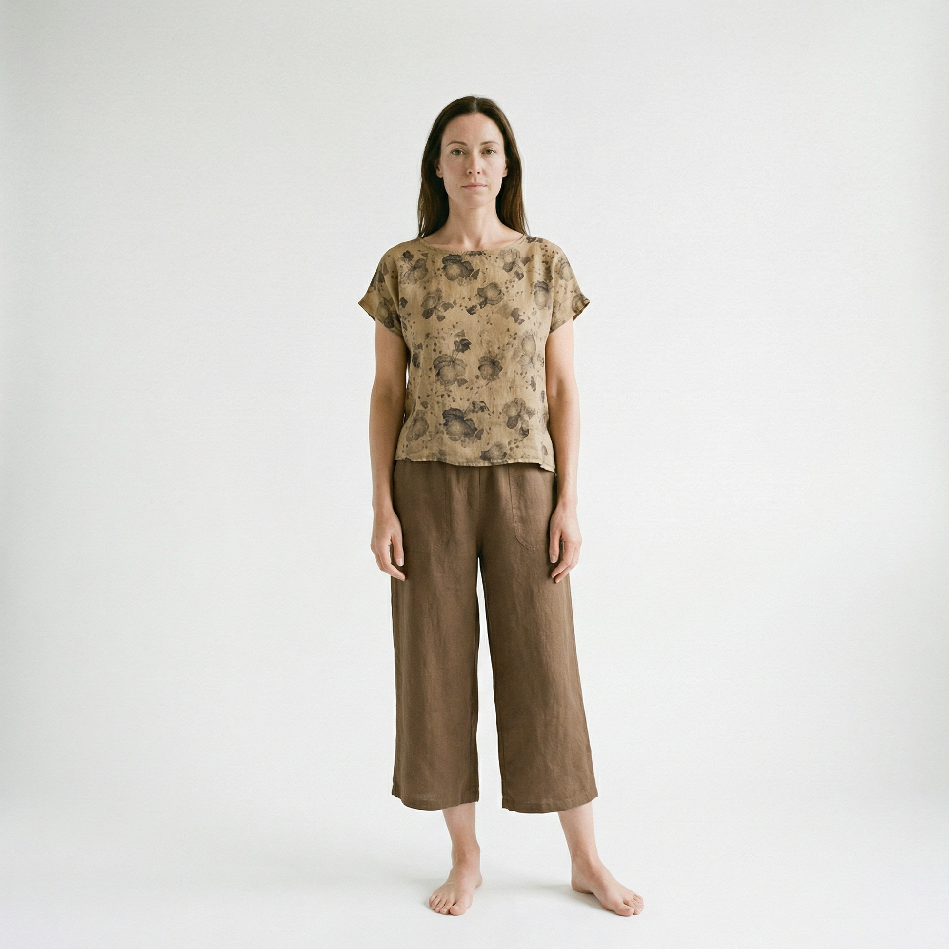 Woman wearing a patterned top and brown pants on a white background